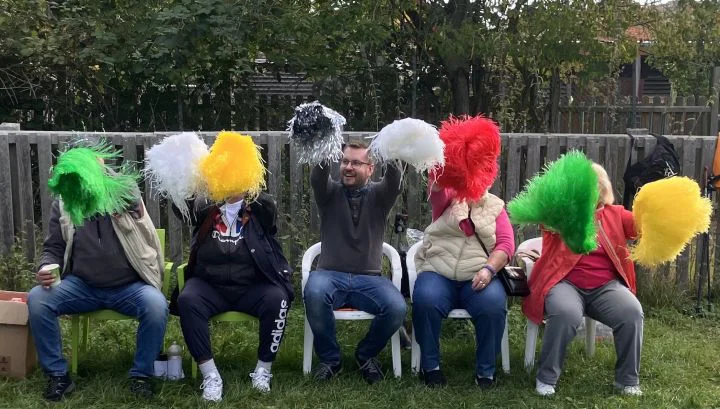 Puscheltruppe Maenner auf einer Parkbank schwenken bunte Puschel